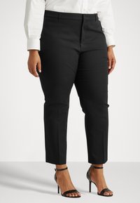 Pantaloni neri su misura con taglio dritto, texture liscia e tasche frontali, abbinati a sandali con tacco alto neri e cinturini.