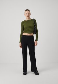 Olive green, ribbed long-sleeve crop top with drawstring sides, paired with black, wide-leg pants. Footwear features chunky black sole.
