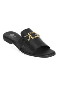 Sandales en cuir noir avec une large sangle ornée d'une boucle dorée et une semelle plate. Surface texturée avec un intérieur lisse.