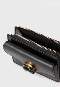 Musta nahkalompakko, jossa on kullanvärinen vetoketju. Lompakossa on kaksi lokeroa ja etuosassa koristeellinen kulta-musta yksityiskohta. Sileä pinta.