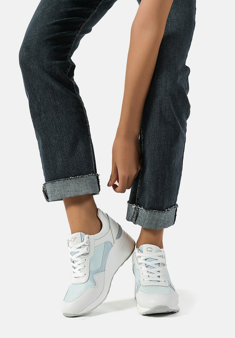 Sneaker bianche e azzurre chiare realizzate in mesh e pelle, con design lacciato e suola rialzata. Abbinate a jeans scuri con risvolto.