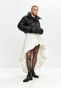 Doudoune noire à finition brillante, jupe asymétrique blanche, collants en dentelle noire à motif floral et bottines en cuir noires.