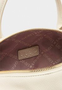 Interno di una borsa in pelle crema con zip dorata, rivestimento rosa chiaro con logo "LIU JO" ripetuto e etichetta di marca cucita all'interno.
