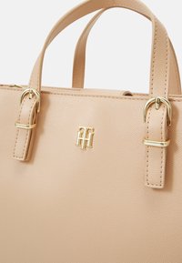 Sac à main en cuir texturé marron avec deux poignées courtes, des accents en métal doré et un logo embossé à l'avant.