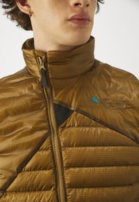 Brown puffer jacket with a high collar, featuring a zip closure, textured fabric, and black mesh accent on the chest. Blue logo displayed.