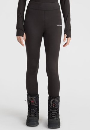 Schwarze Sportleggings mit hohem Bund und glatter Textur, die auf der linken Hüfte ein kleines Logodetail aufweisen. Getragen mit schwarzen Stiefeln.