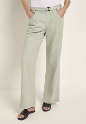 Blassgrüne weite Hosen mit einem Gürtel, ausgestattet mit Seitentaschen und einer glatten Textur. Getragen mit schwarzen Riemchensandalen.