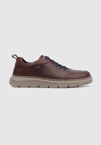 Zapatilla de cuero marrón con cordones azul marino, suela de goma con acentos texturizados. Etiqueta de la marca visible en el lateral. Diseño de perfil bajo.