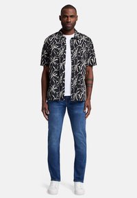 Svart kortärmad skjorta med vitt blommönster, kombinerad med blåjeans och vita sneakers. Skjortan har en button-down krage.