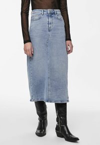 Jupe midi en denim bleu clair avec une silhouette droite, taille haute et poches avant partielles, associée à des bottes en cuir noir montantes.