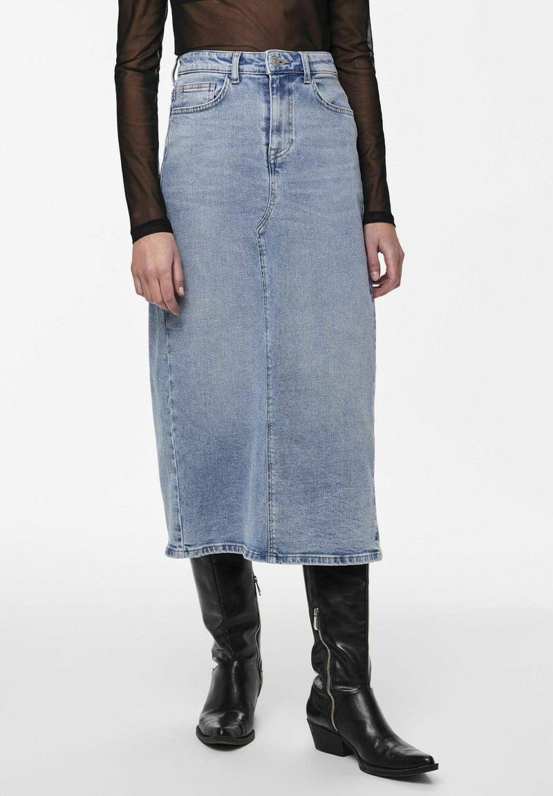 Jupe midi en denim bleu clair avec une silhouette droite, taille haute et poches avant partielles, associée à des bottes en cuir noir montantes.