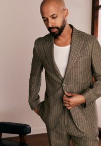 Brown striped suit made of textured fabric, featuring a single button closure, notch lapels, and a white undershirt.