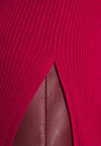 Gros plan d'un tissu tricoté rouge côtelé chevauchant une surface en cuir bordeaux avec des coutures visibles.