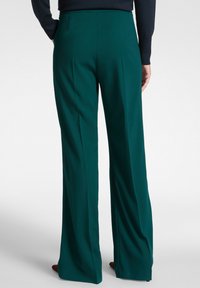 Pantaloni a gamba larga in tessuto verde scuro, con una superficie liscia, design sartoriale, tasche laterali e sottili pieghe frontali.