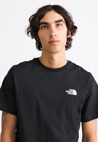 Sort bomulds T-shirt med korte ærmer, rund hals og hvidt logo på venstre bryst. Glat tekstur, afslappet pasform.