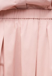 Απαλό ροζ φούστα με ελαστική ζώνη μέσης και διακριτικές πιέτες σε ελαφρύ ύφασμα.