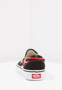 Mustat liukupohjaiset lenkkarit, joissa on punaisia ja oransseja liekkikuvioita, valkoinen kumipohja ja Vans-logo takana. Kangasmateriaali, pyöristetty muoto.