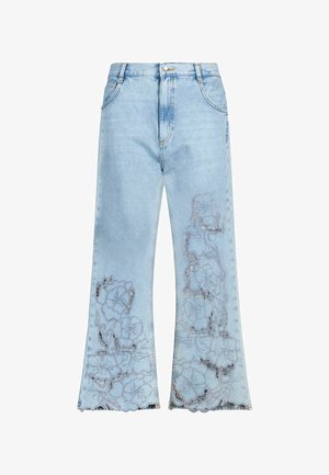 Hellblaue Jeans aus Denim mit ausgestellten Beinen und floraler Spitze mit ausgeschnittenem Stickmuster an beiden Beinen nahe dem Saum.