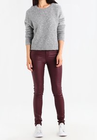 Szary, luźny sweter z dzianiny o okrągłym dekolcie, w połączeniu z bordowymi, dopasowanymi spodnie z ekologicznej skóry oraz białe trampki.