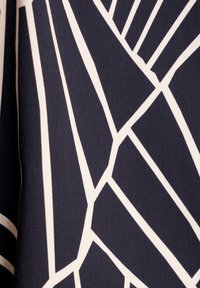 Tissu bleu marine avec de grandes lignes géométriques blanches abstraites formant un motif audacieux. La texture semble lisse et ferme.