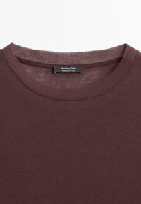 Gros plan sur un t-shirt col rond couleur bordeaux avec une étiquette noire à l'intérieur du col indiquant "Massimo Dutti Made in Portugal".