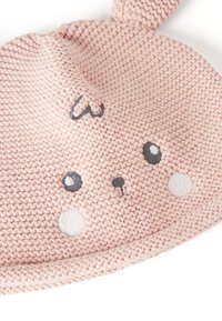 Pletená růžová čepice s designem králičí tváře, která má vyšívané oči a nos, a dva akcenty ve tvaru uší na vrcholu.