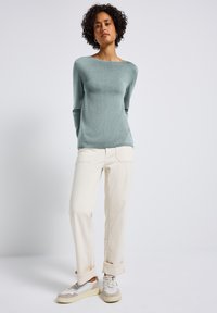 Maglione verde chiaro a maniche lunghe con scollatura rotonda, abbinato a pantaloni crema a vestibilità ampia e sneakers beige con dettagli bianchi.