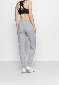 Zwarte sportbeha met een design van riempjes aan de achterkant, gecombineerd met lichtgrijze, taps toelopende joggingbroeken. Model draagt witte sneakers met grijze accenten.