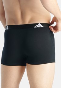 Svarta tight boxer shorts med en slät yta, som har en vit logotyp på den elastiska midjebandet och en åtsittande, formad design.