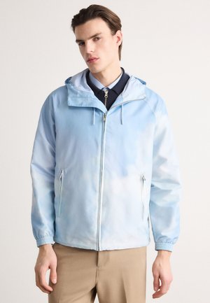 Hellblaues Kapuzenjacke mit einem verlaufenden Wolkenmuster, Reißverschluss vorne und seitlichen Taschen, elastischen Bündchen und einer glatten Stofftextur.