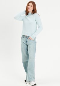 Lys blå strikket sweater med høj hals, parret med lyse denim bukser med vide ben. Hvide sneakers fuldender outfittet. Glat tekstur, afslappet stil.