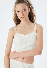 Camisola bianca in cotone con delicati dettagli in pizzo, caratterizzata da strisce verticali e piccoli motivi ricamati. Design semplice e aderente.