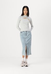 Cămașă lungă cu mânecă lungă de culoare gri deschis, cu detalii decupate, asortată cu o fustă midi din denim albastru deschis, care are o fante în față și margini desfăcute.