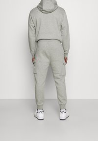 Grå bomullshuvtröja och cargo-sweatpants med elastiska muddar och sidofickor, matchat med vita sneakers, sedd bakifrån.