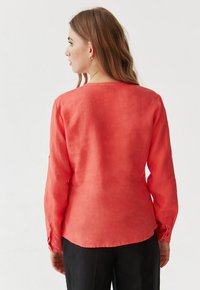 Camicia di lino corallo a maniche lunghe con collo rotondo e polsini abbottonati, con taglio dritto sul retro e texture liscia.