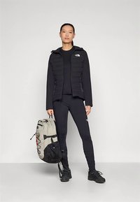 Fekete bélelt dzseki cipzáras elején, hozzáillő fekete felsővel és leggingsszel. Világosszürke hátizsák fekete részletekkel. Fekete lábbeli.