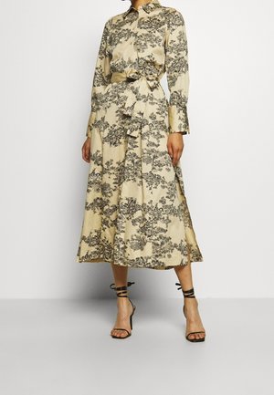 Robe à manches longues, avec boutons, en beige clair avec un motif floral noir. Dotée d'une taille ceinturée et d'un ourlet fluide jusqu'aux chevilles.
