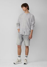 Camicia a righe con colletto alla mandarino, abbinata a pantaloni corti in denim grigi chiari e sneakers chiare con calzini a righe bianche e nere.