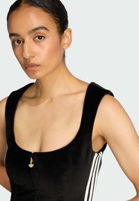 Čierne zamatové šaty s výstrihom do lodičky, zlatým zipsom a bielymi pruhmi po stranách. Hladká textúra a priliehavý strih.