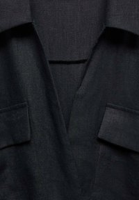 Zwarte gestructureerde blazer met notch-revers en klepzakken aan de voorkant, weergegeven in close-up.