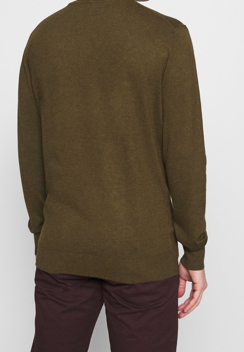 Khaki groene trui met lange mouwen, ronde halslijn en geribbelde zoom. Gestructureerde gebreide stof zorgt voor een zachte afwerking. Gecombineerd met donkerbordeauxrode broek.