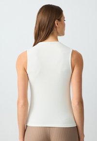 Top bianco a costine senza maniche con collo alto, texture liscia e forma aderente, abbinato a pantaloni marroni a righe.
