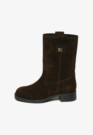 Botte mi-mollet en daim brun foncé avec petit talon et patch logo métallique "MS" près du haut sur fond blanc.