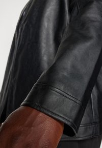 Chaqueta de cuero negro con un diseño estructurado, textura suave y mangas ajustadas con sutiles detalles de costura.