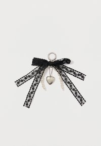 Schwarzes Spitzenband mit einer silbernen Herzanhänger und Perlenakzenten. Es zeigt aufwendige Blumenmuster und unterschiedliche Bänderlängen, die an einer Schlaufe befestigt sind.