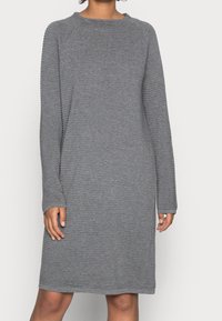 Robe grise en tricot avec une texture côtelée, manches longues et col rond. Coupe décontractée, longueur genoux, détails minimalistes.