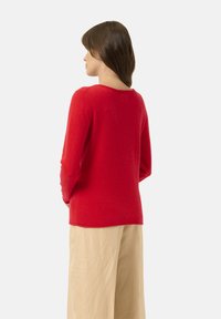 Maglione rosso di lana con maniche lunghe e scollatura tonda. Tessuto morbido e vestibilità leggermente ampia, abbinato a pantaloni in lino beige.