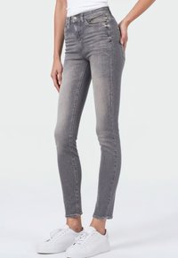 Grijze skinny jeans met een vervaagde afwerking, voorzien van een hoge taille en voorzakken. Gekoppeld aan witte sneakers, wat de slanke pasvorm en het ontwerp benadrukt.