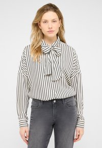 Striped blouse in black and white with a bow tie collar, long sleeves, and button front. Worn with gray jeans, smooth texture.