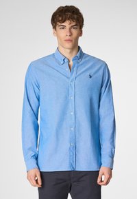 Camicia azzurro chiaro con bottoni realizzata in un tessuto testurizzato, dotata di un colletto classico e un piccolo logo ricamato sul lato sinistro del petto.
